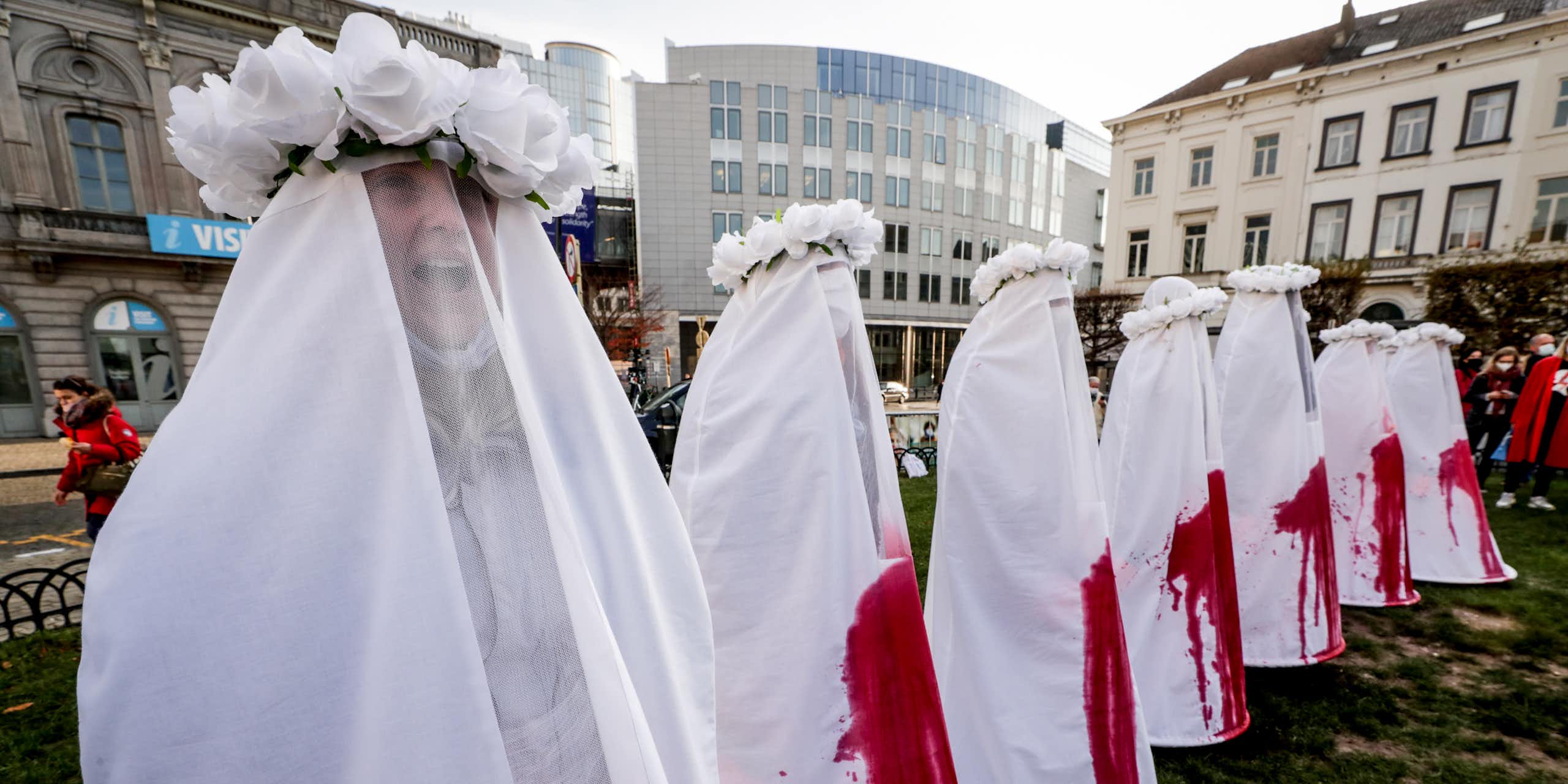Women dressed in white costumes stained with blood stand in a line in Brussels.