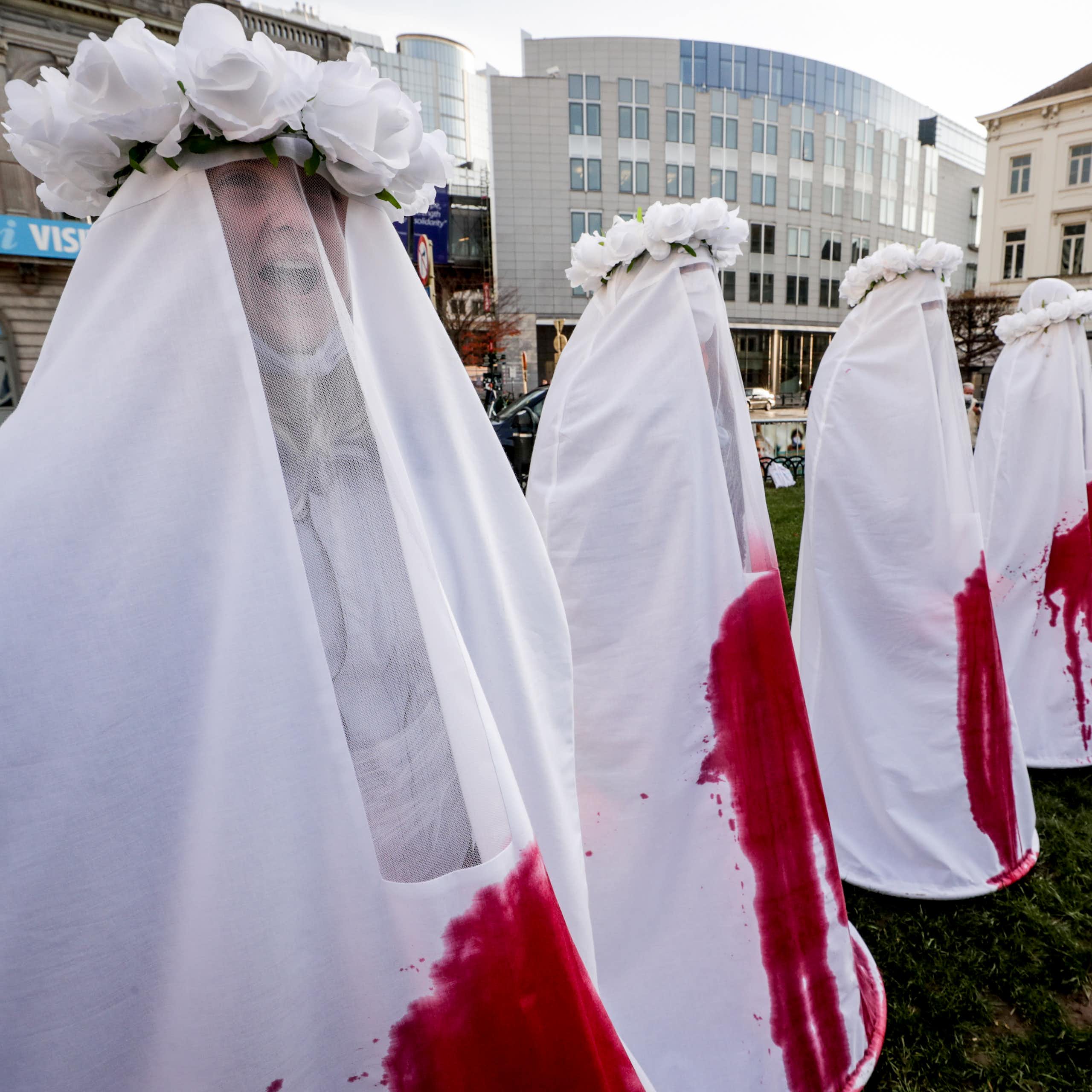 Women dressed in white costumes stained with blood stand in a line in Brussels.