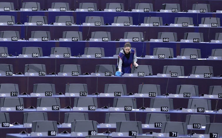 A woman cleans desks in the European Parliament chamber.