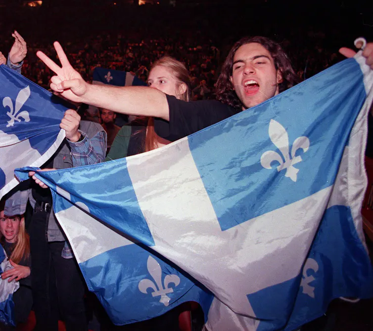 A young man makes the peace sign while holding up the Québec flag.
