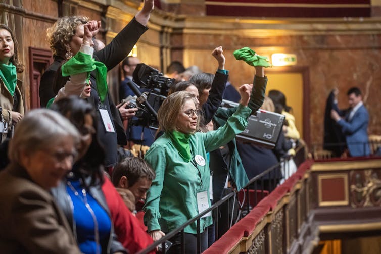 Women wave green scarves on the balcony of an official building.