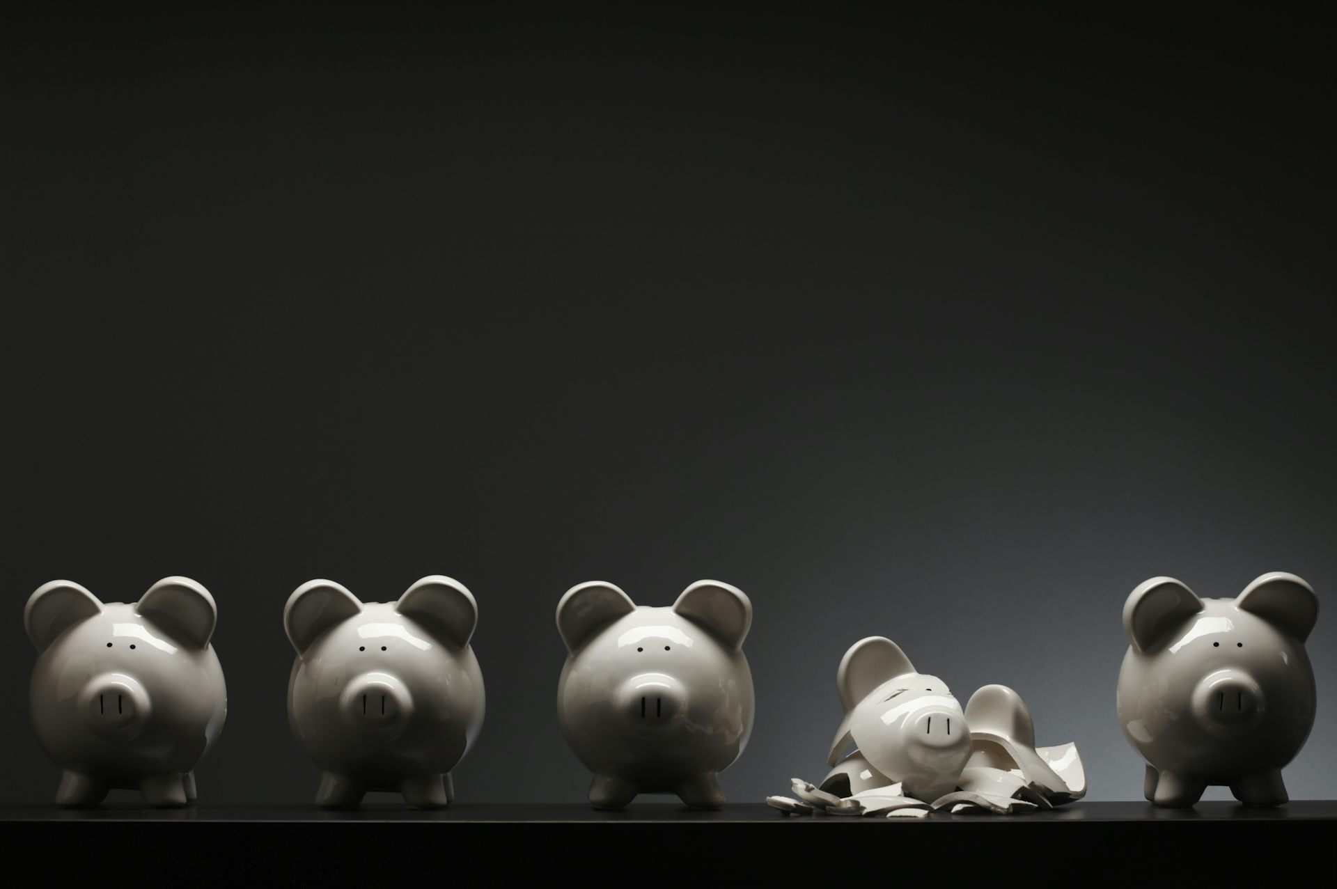 Four ceramic piggy banks and one that is shattered into pieces