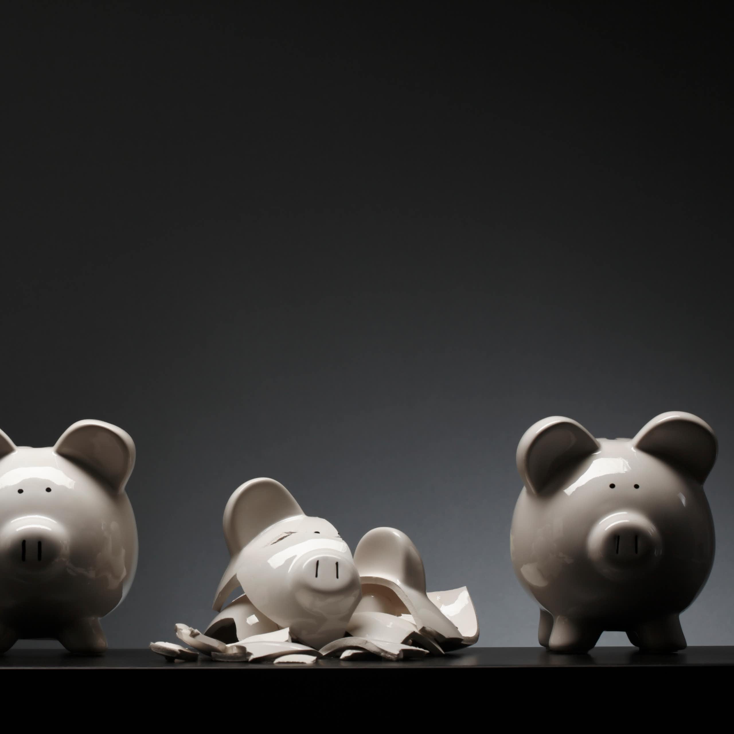 Four ceramic piggy banks and one that is shattered into pieces