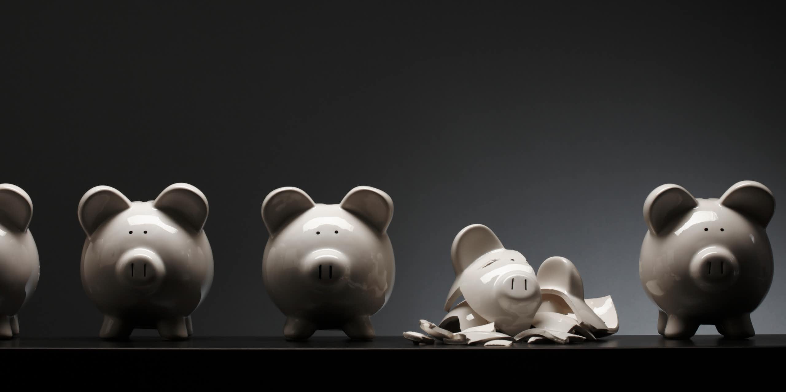 Four ceramic piggy banks and one that is shattered into pieces