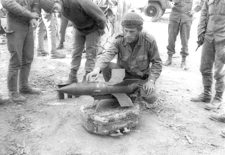 black and white photograph of a man in military uniform crouching beside a missile.