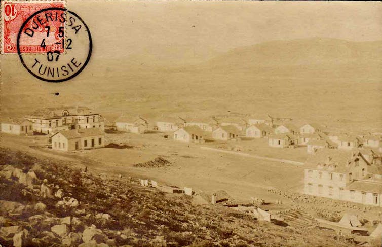 A sepia photograph of an old town, larger buildings on either side and a dozen or so houses between them.