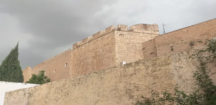 Une grande forteresse carrée se profile au-dessus de hauts murs.