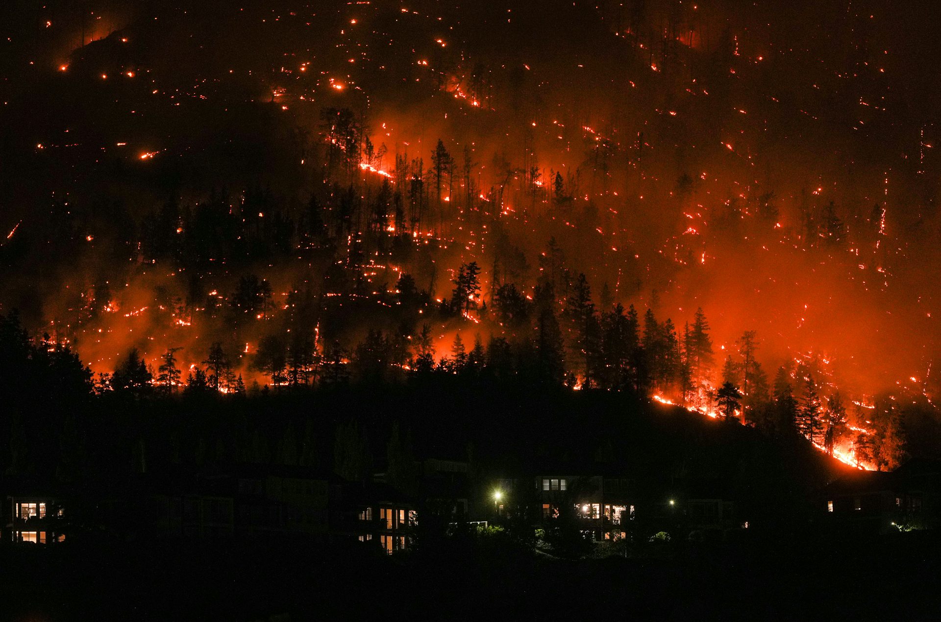 A fire burns in the background with small buildings in the foreground.