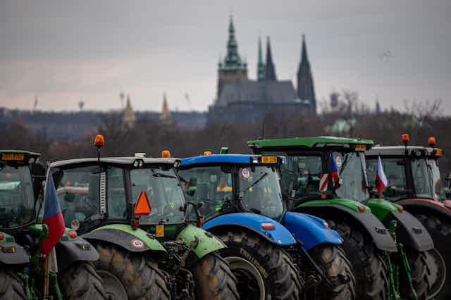 A row of tractors with grand buildings in the distance.