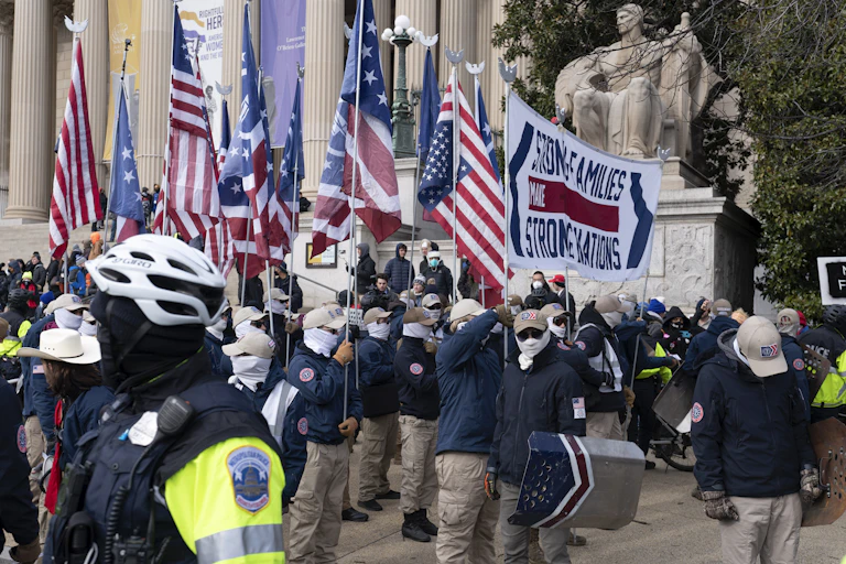 Several men in blue jackets holding American flags outside a building with Corinthian columns and a seated statue.
