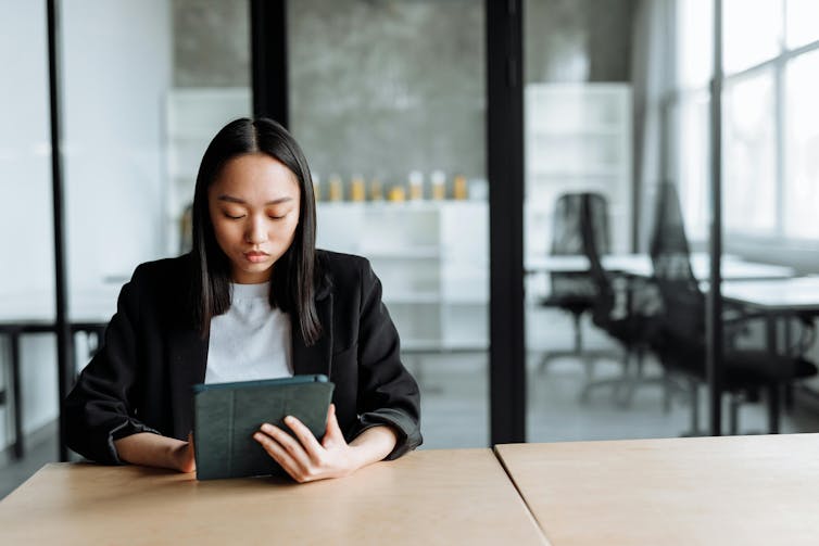 A woman reads an ipad while sitting at a table.
