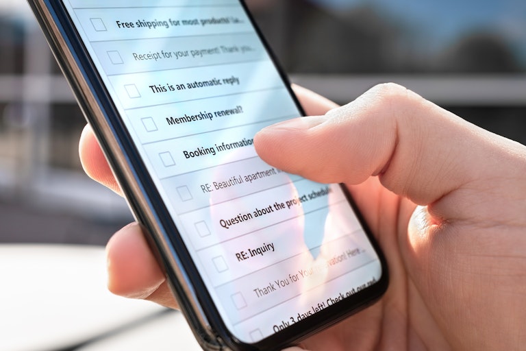 A person holding a smartphone with a list of emails on it.