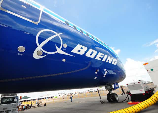 A dark blue plane with Boeing logo on a tarmac being refuelled.