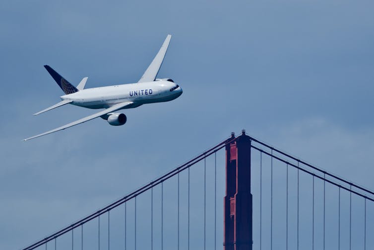 Un avion de United Airlines vu au loin au-dessus d’un pont
