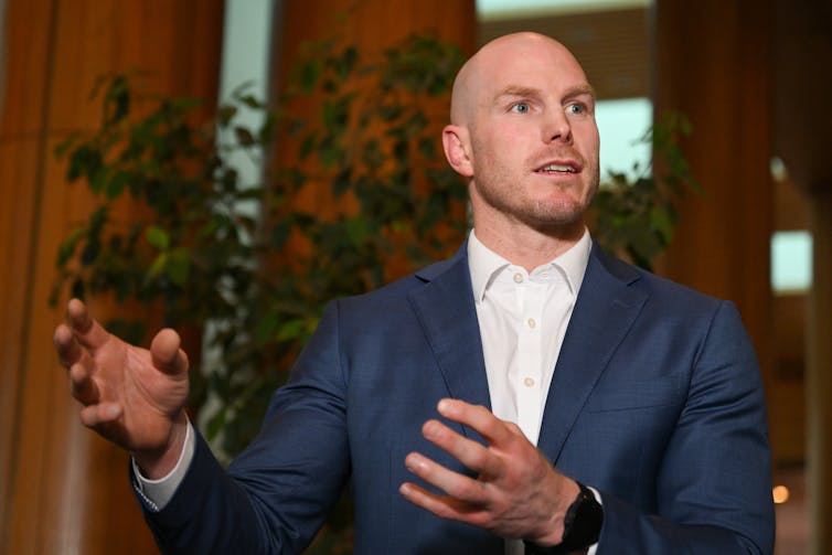 A man in a suit talks and gesticulates at a press conference