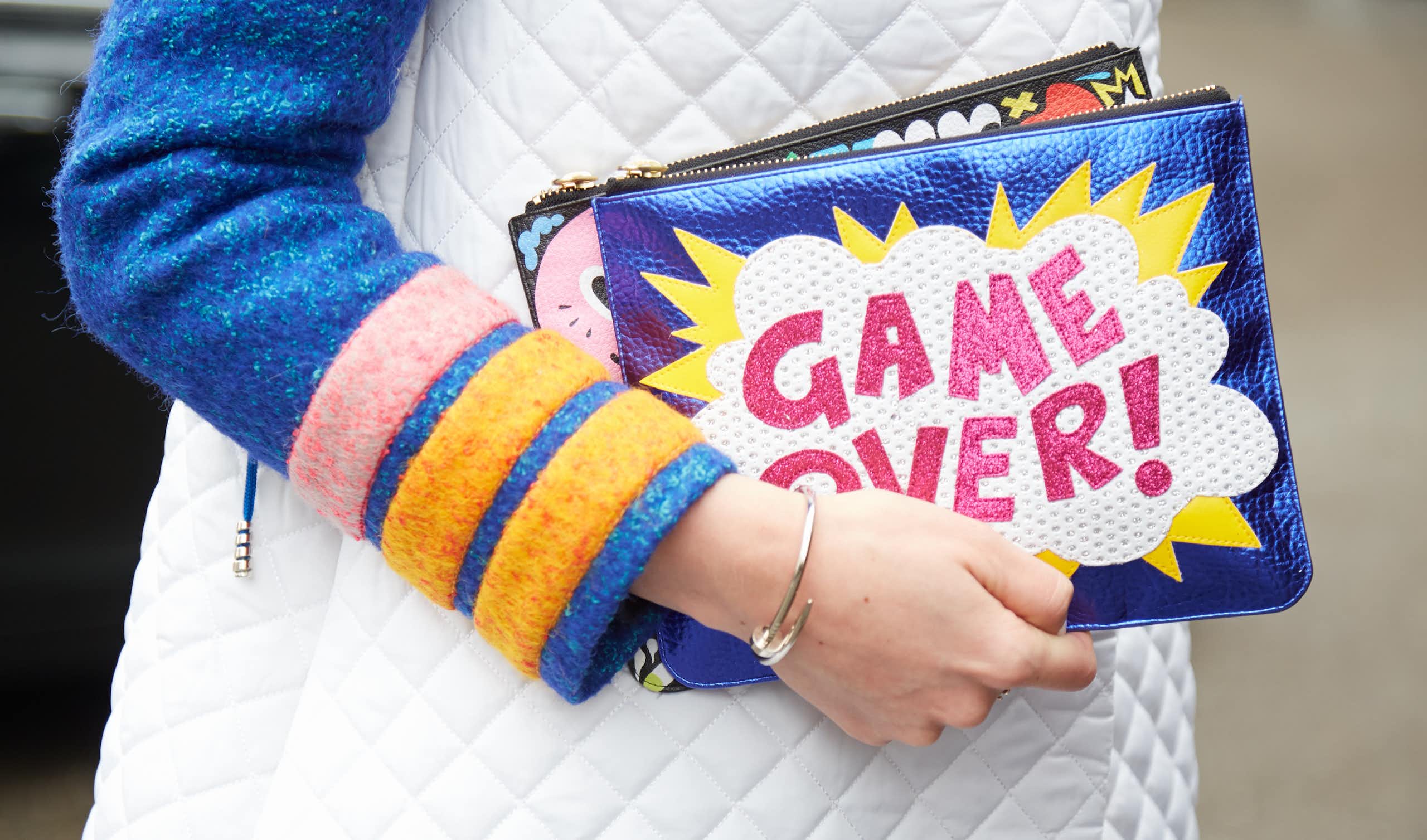 A woman's hand holding a clutch bag that says "GAME OVER!"