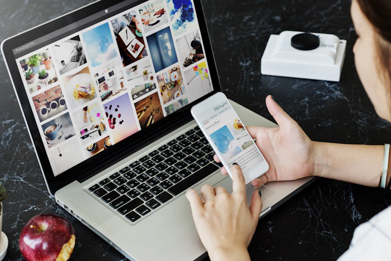 a woman holds a mobile phone while sitting in front of a laptop
