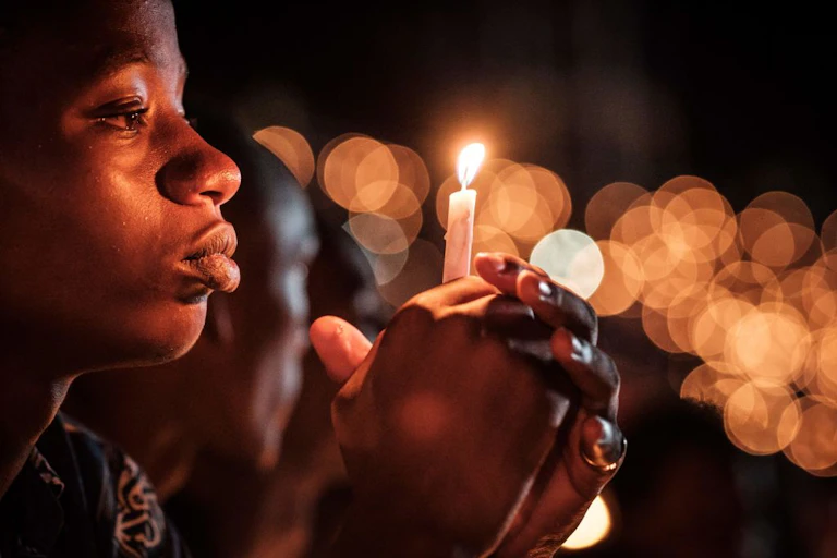 A young person holding a candle in the foreground with gold circles in the background showing other lit candles out of focus