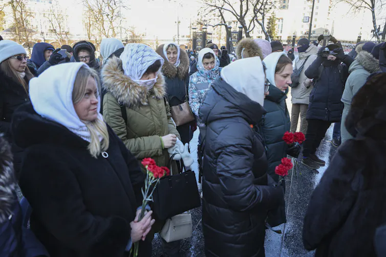 Russian women in headscarves holding bunches of flowers.
