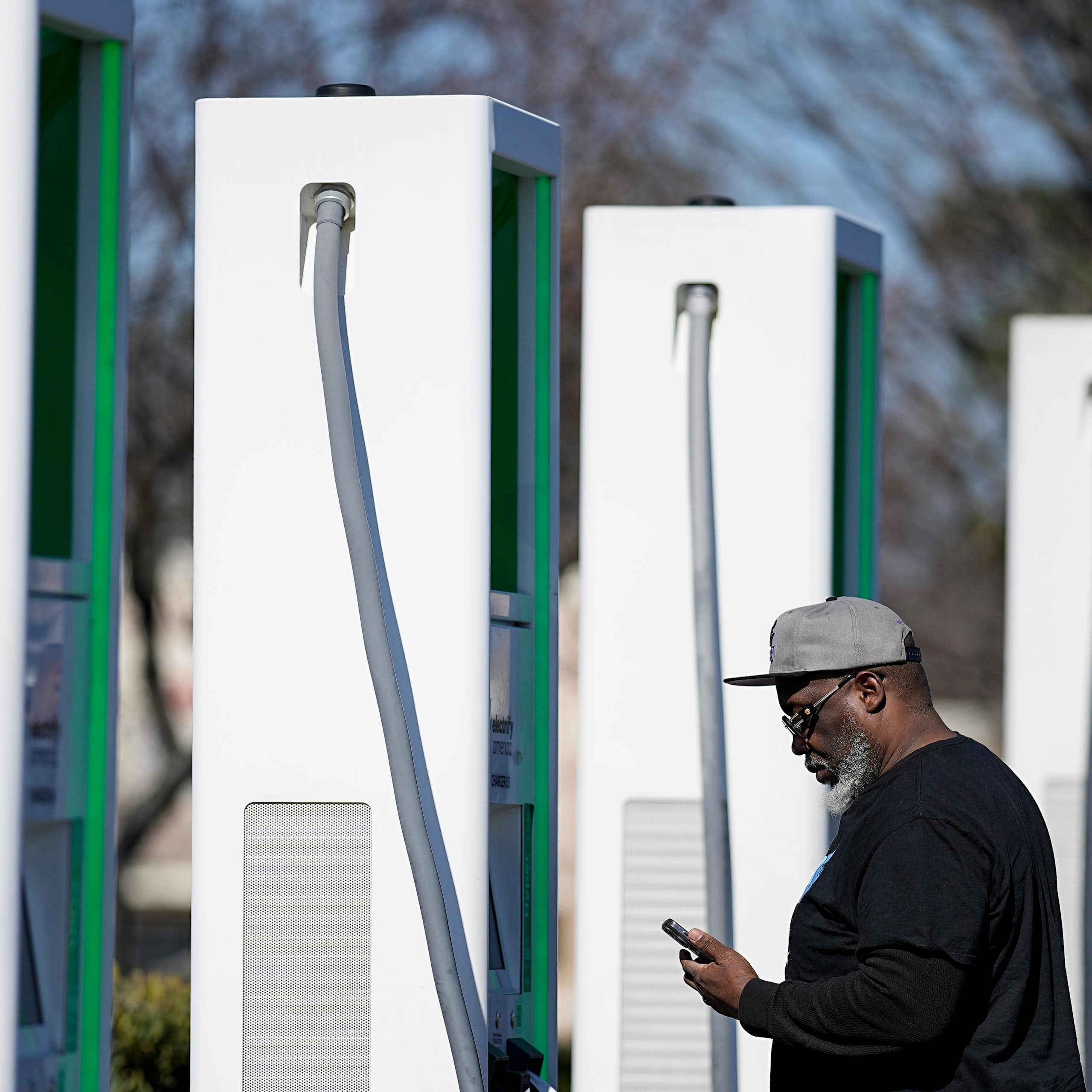 A man stands looking at his phone next to a row of EV chargers.