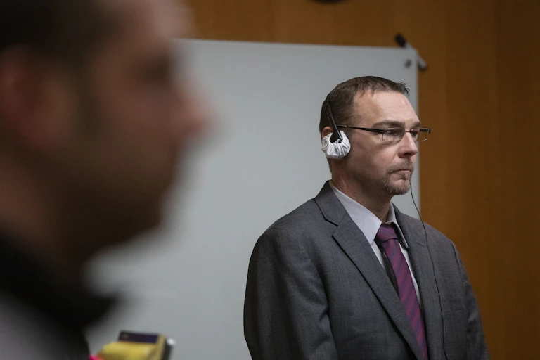 A white man dressed in a business suit is looking straight ahead while listening to testimony.