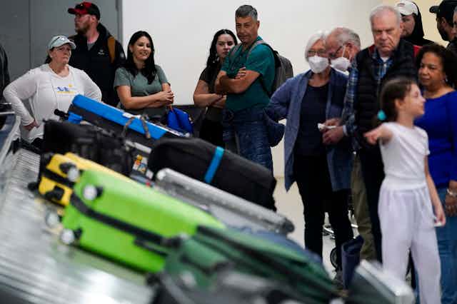 A crowd gathers around an airline baggage claim filled with luggage.