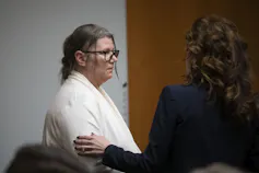 A white woman sits behind a desk while a jury deliberates her fate in another room.