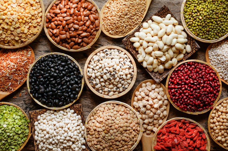 Flatlay shot looking down over a dozen or so colourful bowls of different beans, pulses, legumes