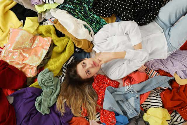Young woman lying on pile of different clothes, top view. 
