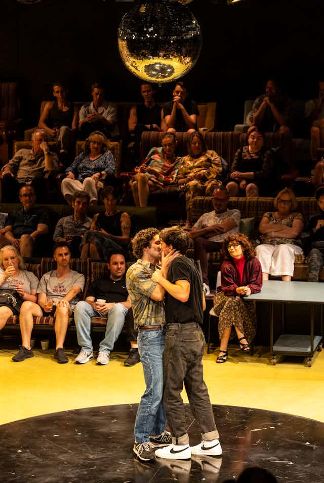 Two men kiss in front of an audience