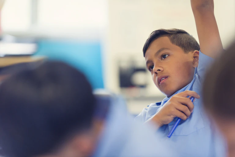 A boy raises his arm in a classroom