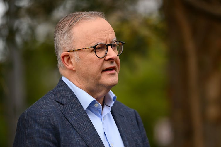 A man stands and talks in front of a green background