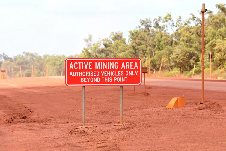 A photo of a sign reading ACTIVE MINING AREA in a red dirt field.