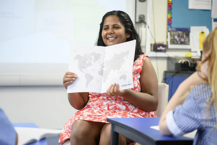 A teacher holds a world map up to a class.