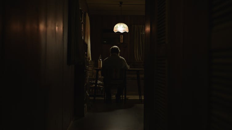 A man sits at a table at the end of a hallway.