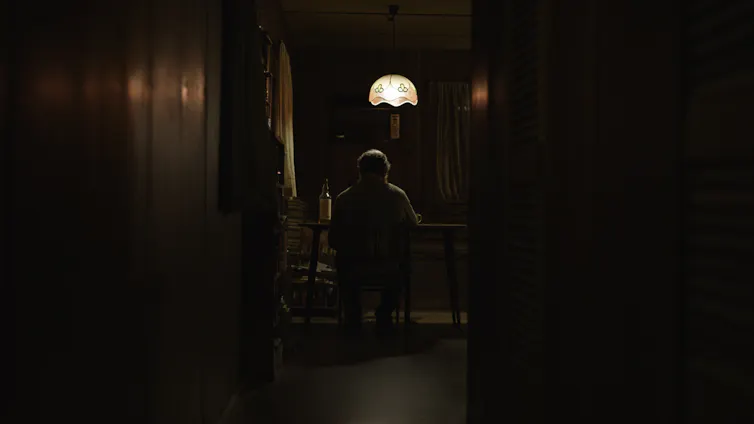 A man sits at a table at the end of a hallway.