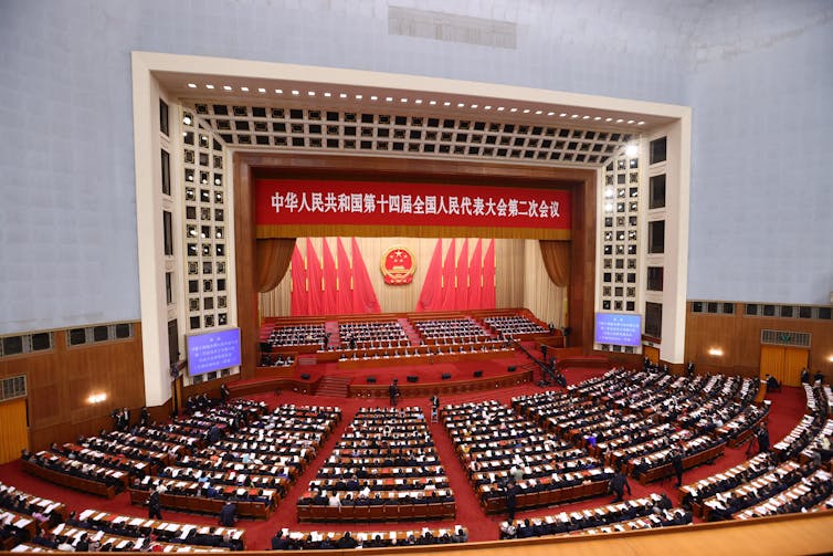 A view of a room full of people in China sat facing a stage.