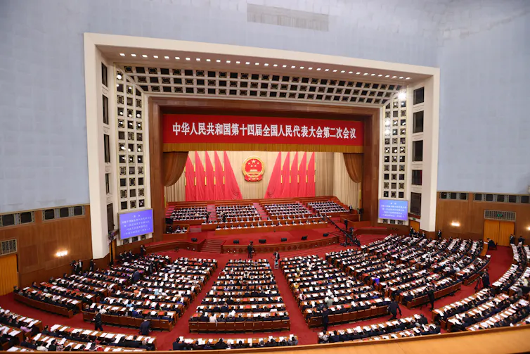 A view of a room full of people in China sat facing a stage.