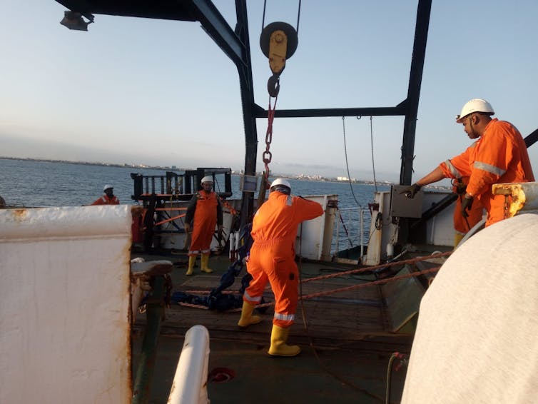 A group of people in orange overalls and white hard hats work on a ship's deck
