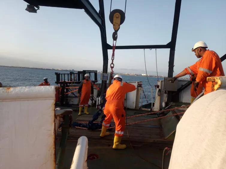 Un groupe de personnes vêtues de combinaisons orange et de casques blancs travaillent sur le pont d'un navire