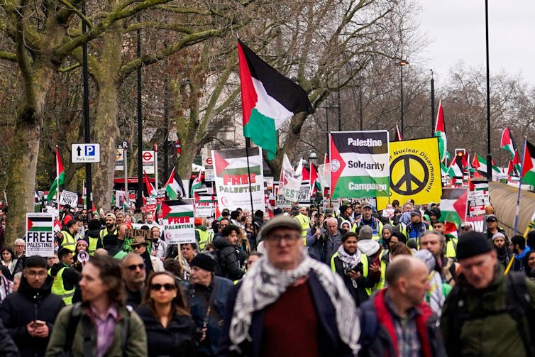 A crowd of protesters marching, waving Palestinian flags and holding signs that read 'free Palestine'.