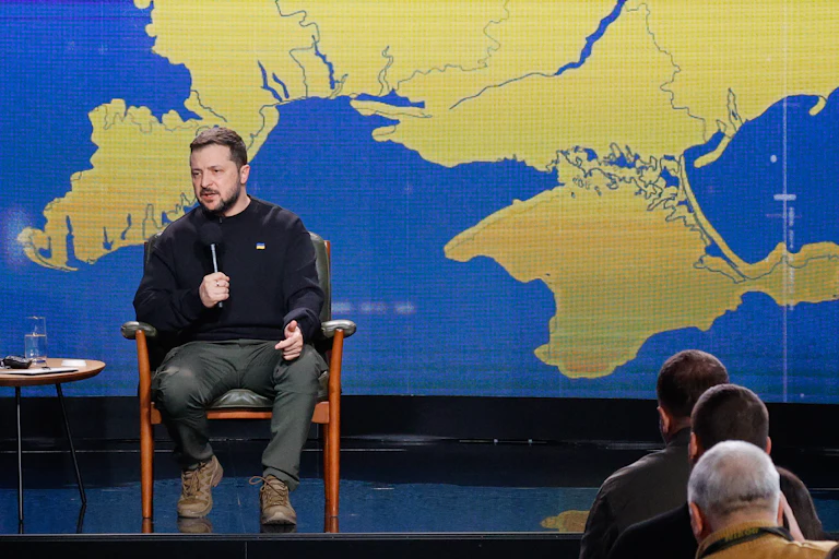 Volodymyr Zelensky talks into a microphone while sitting in front of a map of Crimea