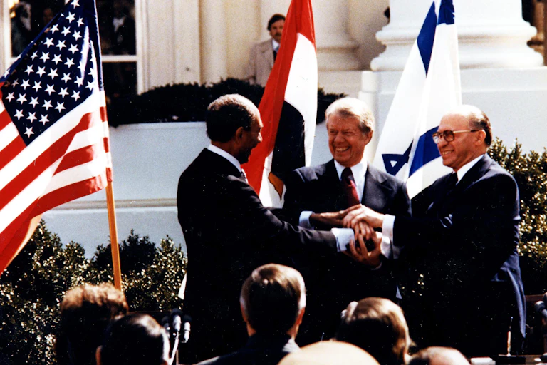 Three men shake hands in front of the White House: Anwar El Sadat, Jimmy Carter and Menachem Begin at the White House, to sign the 1979 Egypt–Israel peace treaty.