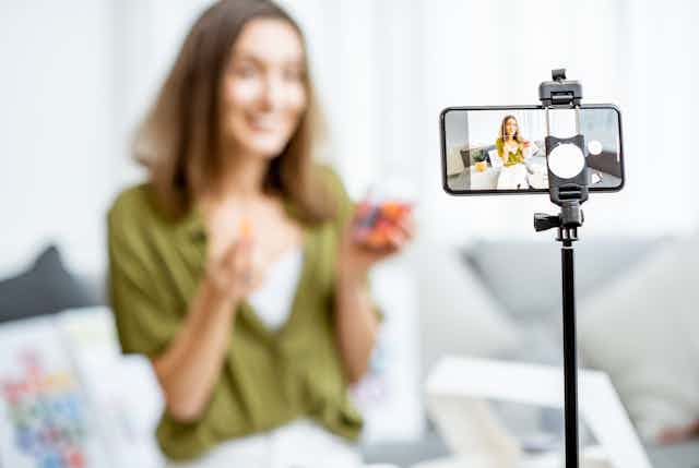 A woman out of focus recording video on a smartphone in the foreground