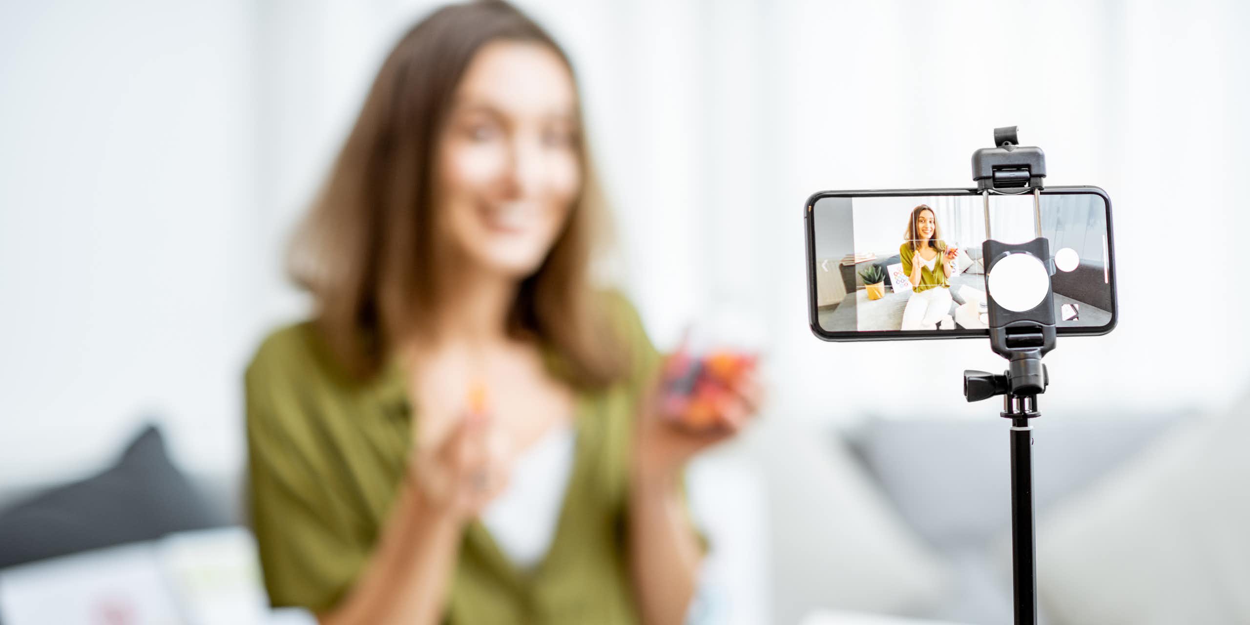 A woman out of focus recording video on a smartphone in the foreground