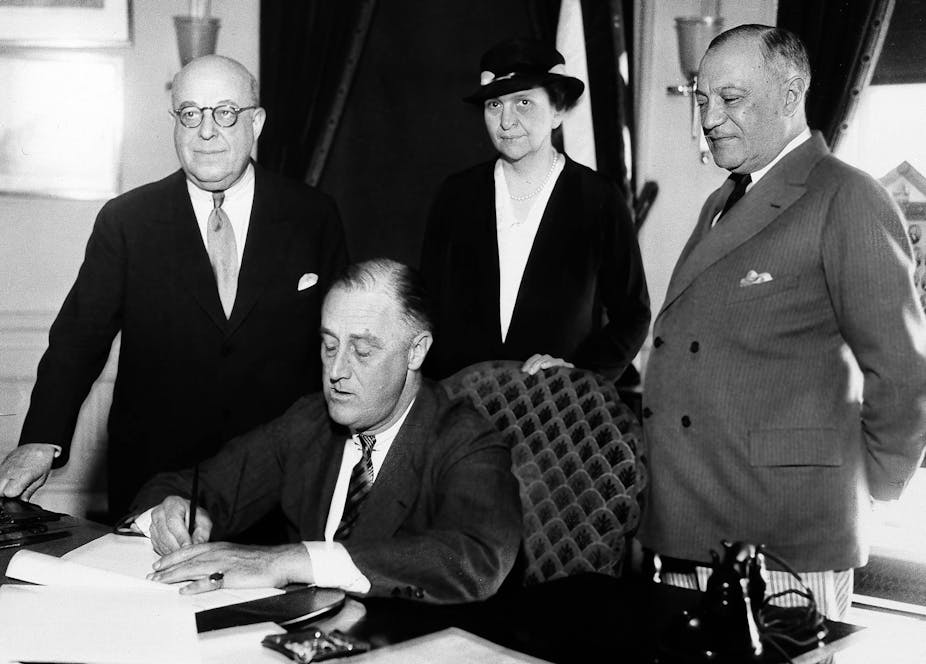 FDR signs a bill into law in an old black and white photo.