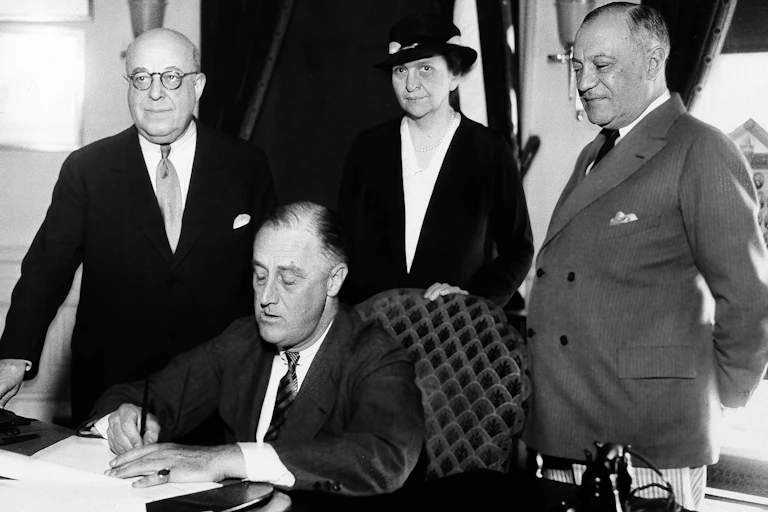 FDR signs a bill into law in an old black and white photo.