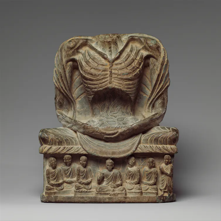 A headless statue of an emaciated person, revealing the ribcage, tendons and veins, with human figures at its base.