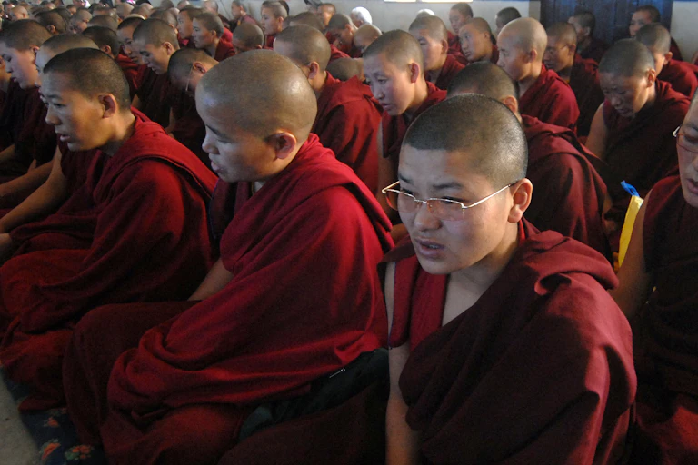 Female monks dressed in maroon robes, seated in rows.