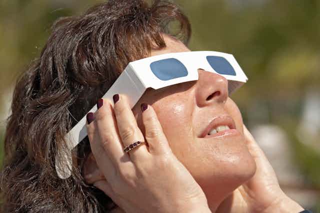 A woman looks at the sun during a total eclipse through mylar solar viewing glasses.
